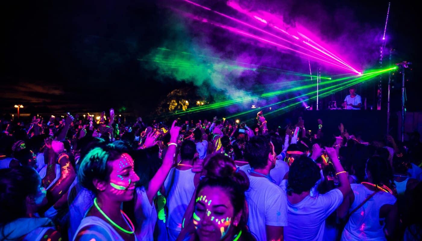 Foule dansant avec des peintures corporelles fluo sous lumières UV et lasers à Festichola